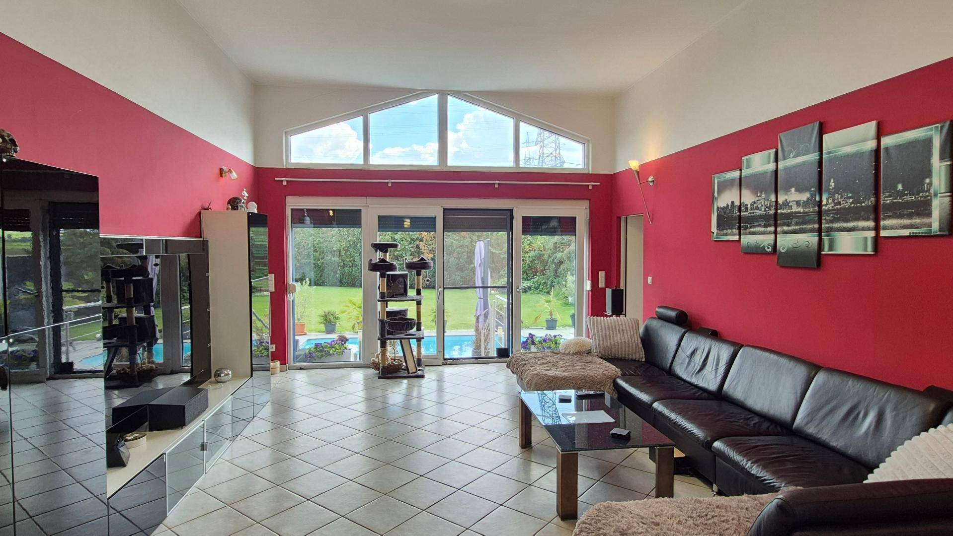 Helles Wohnzimmer mit großen Fenstern, roter Akzentwand und Blick auf den Pool.