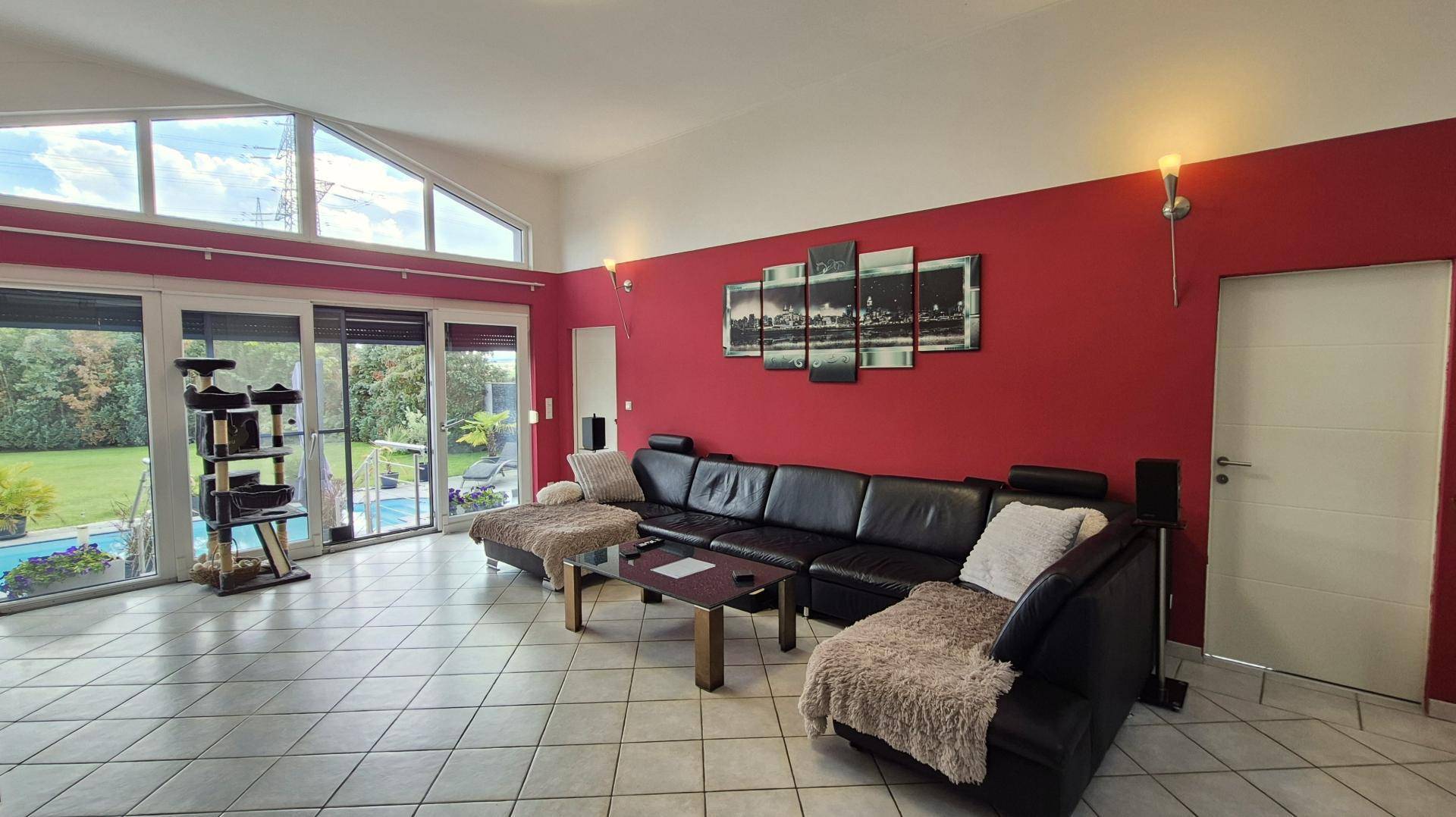 Großzügiges Wohnzimmer mit roten Akzentwänden, großen Fenstern und Blick auf den Garten und Pool.