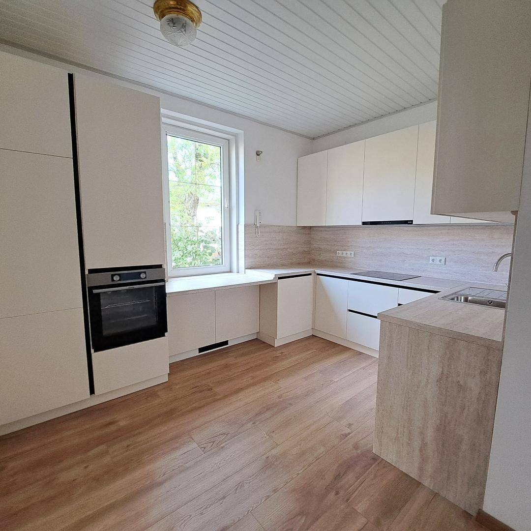 Moderne Einbauküche mit weißen Schränken, integriertem Backofen und Fenster mit Blick ins Grüne.