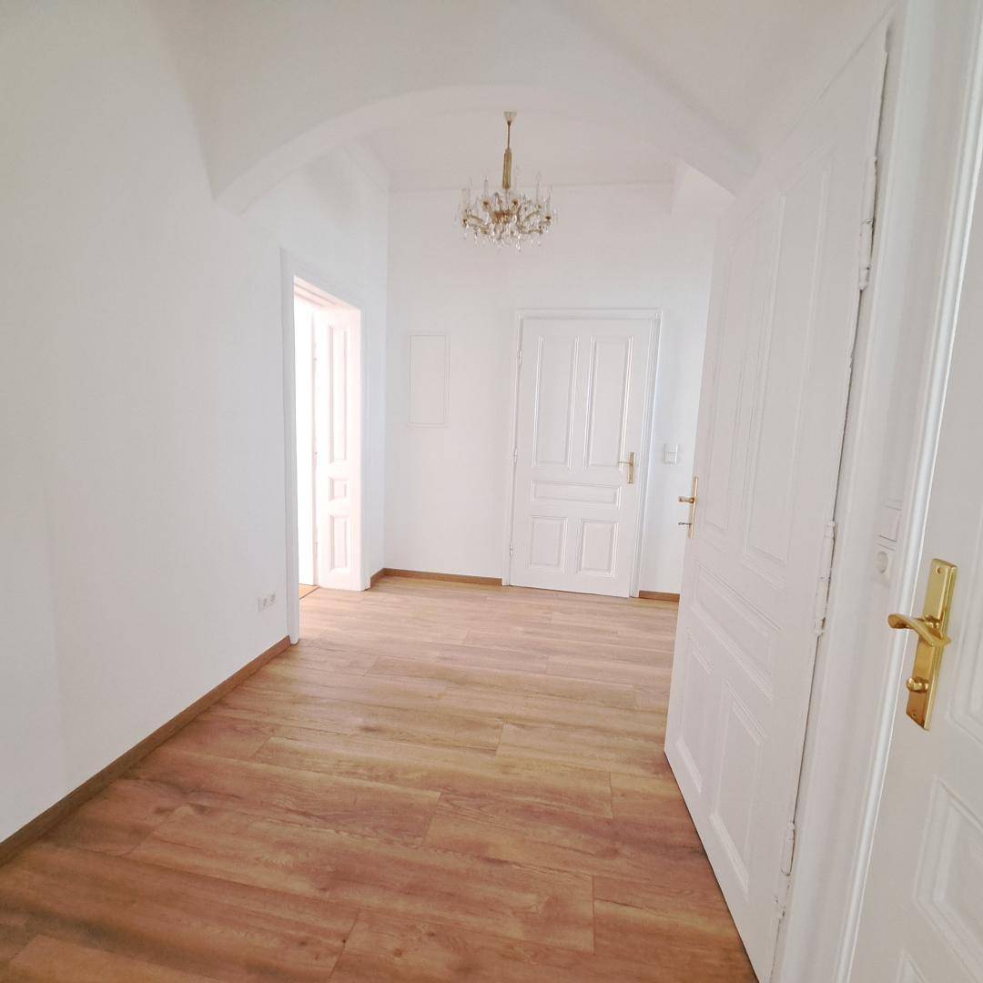 Heller Flur mit Holzboden, weiß gestrichenen Wänden und einem eleganten Kronleuchter.