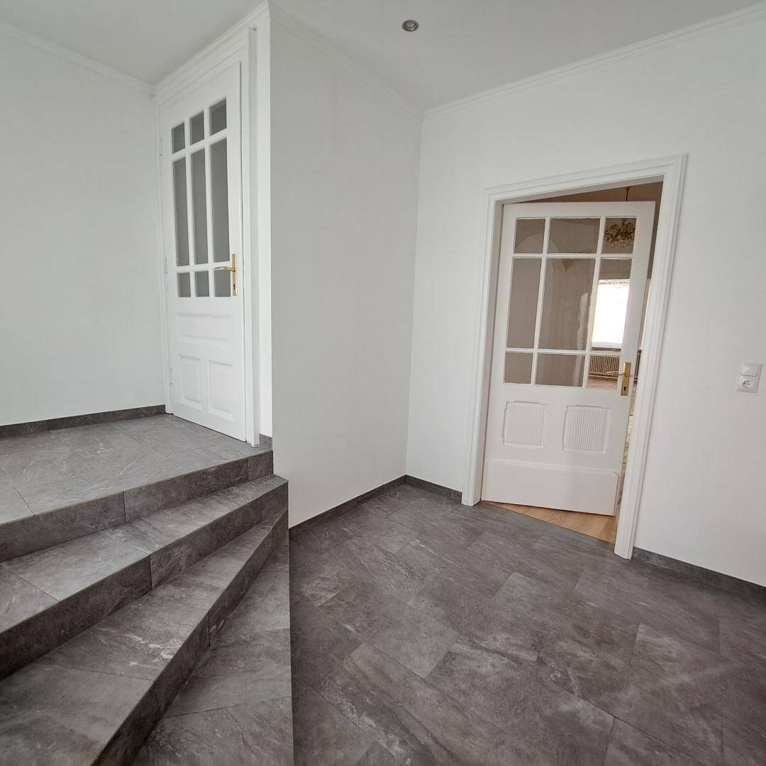 Heller Eingangsbereich mit Steintreppe, Fliesenboden und weißen Türen.