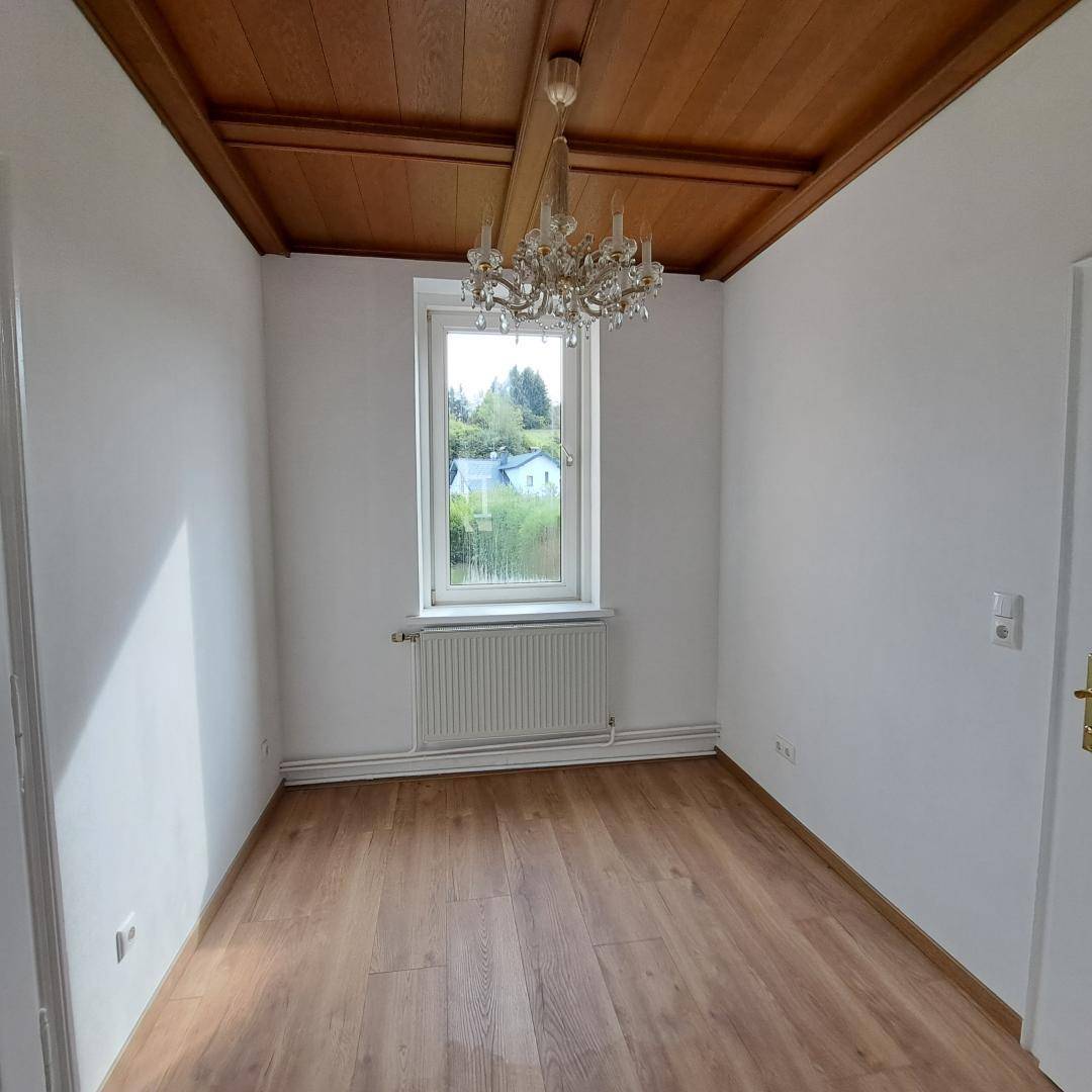Gemütliches Zimmer mit Holzboden, Holzdecke und einem Fenster mit Blick ins Grüne.