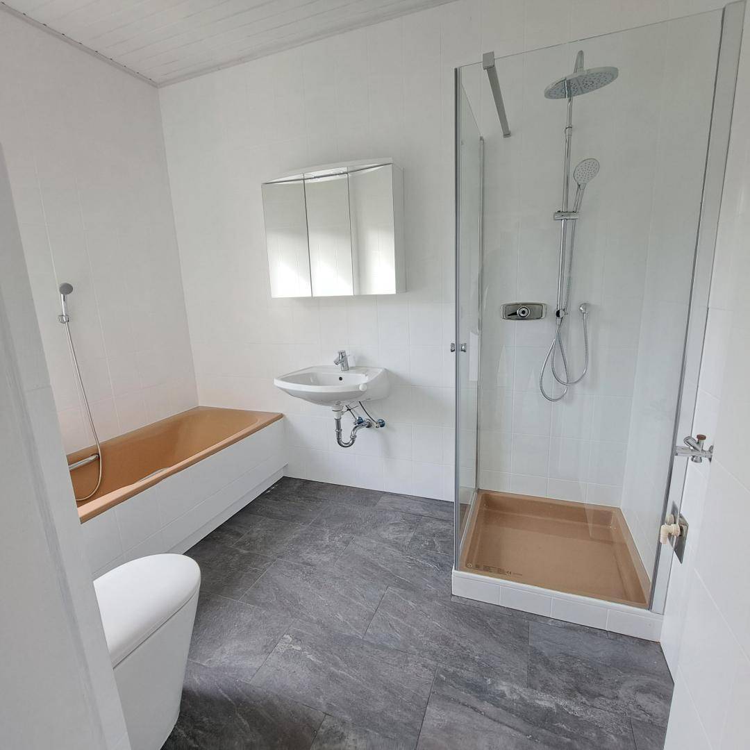 Modernes Badezimmer mit Badewanne, Duschkabine und grauem Fliesenboden.