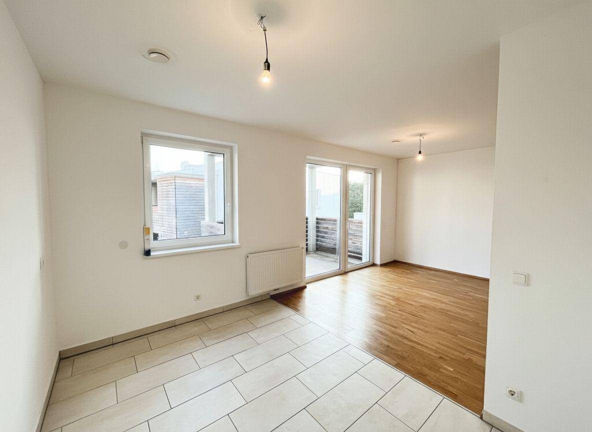Geräumiger Raum mit geteiltem Bodenbelag, Fenster und Balkonzugang.
