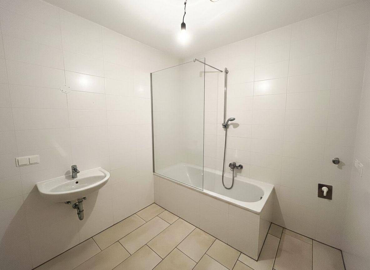 Modernes Badezimmer mit weißen Fliesen, Badewanne mit Duschwand und Waschbecken.