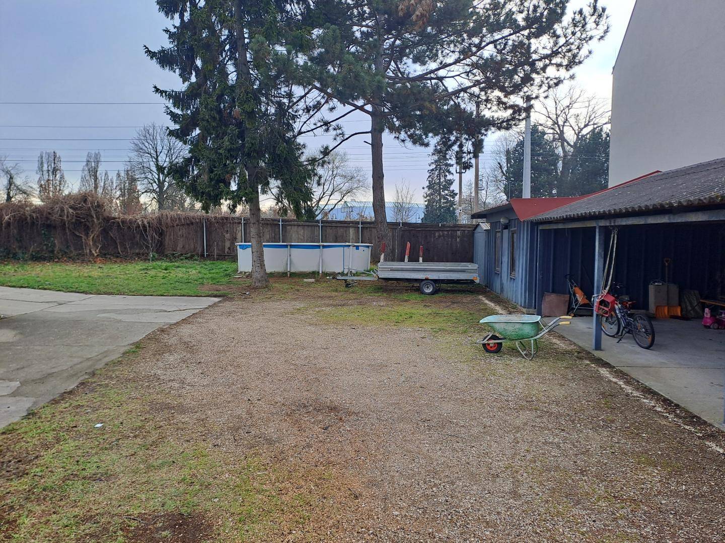 Blick auf den hinteren Gartenbereich mit oberirdischem Pool, Anhänger und überdachtem Stellplatz.