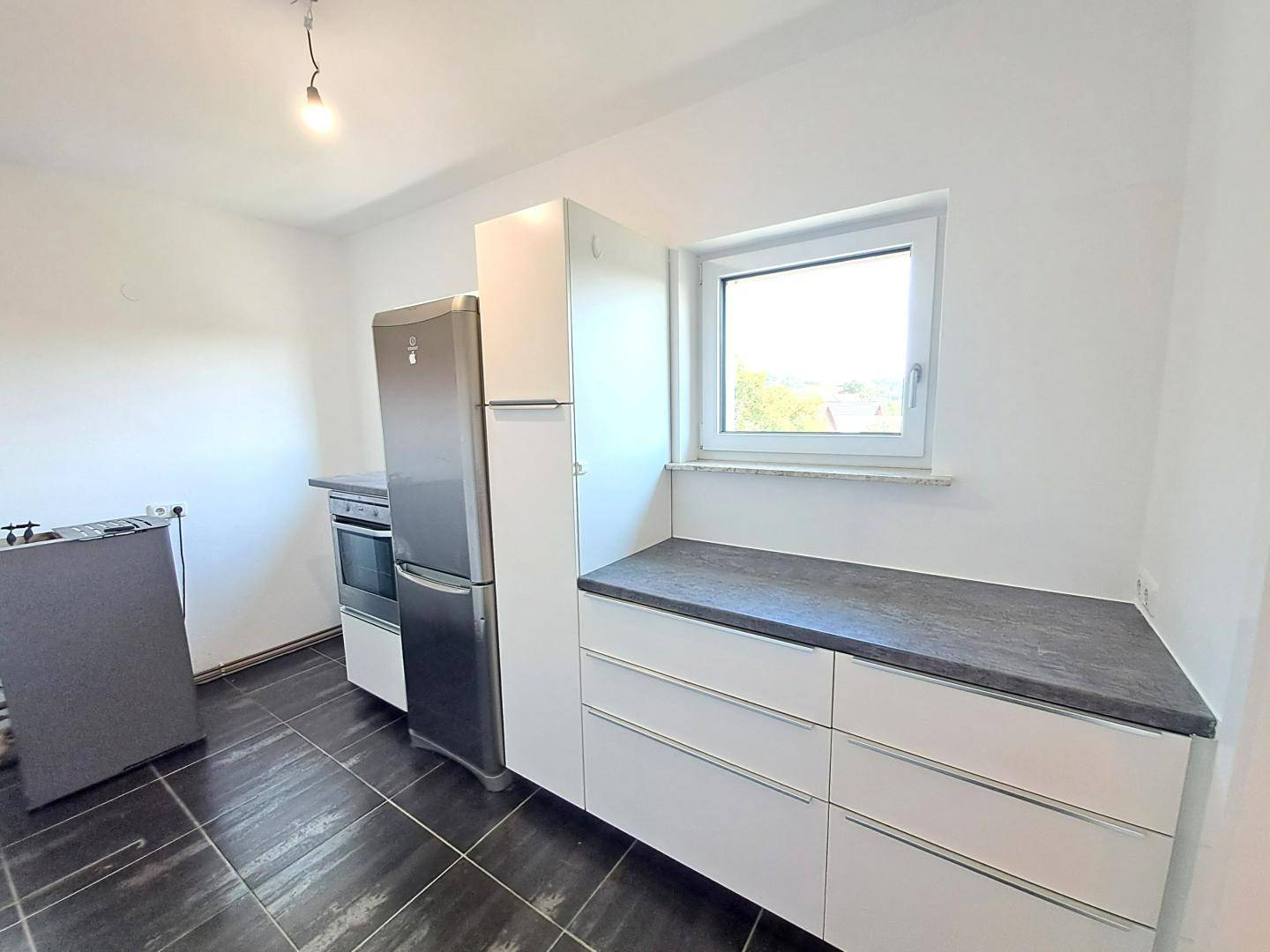 Funktionale Küche mit weißen Schränken, dunkler Arbeitsplatte und Fenster mit Ausblick.