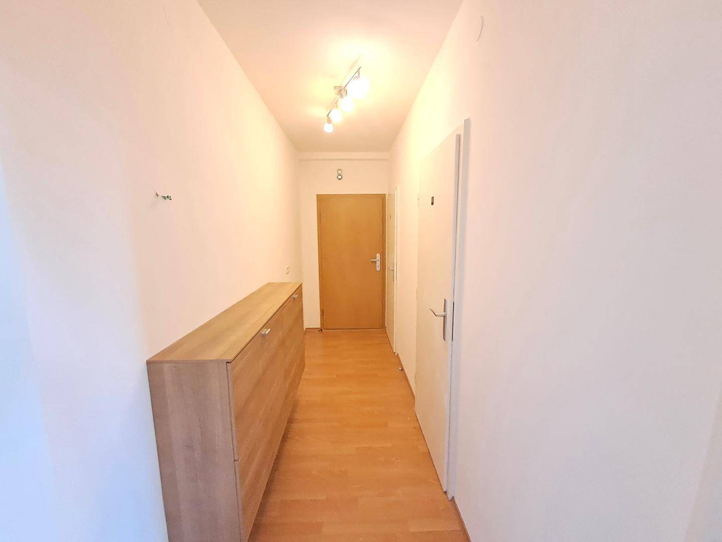 Heller Flur mit Laminatboden und praktischem Schuhschrank, der zu den Zimmern führt.