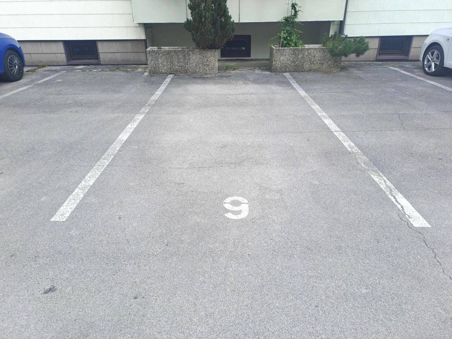 Zugeordneter Außenstellplatz Nummer 9 auf asphaltiertem Parkplatz vor dem Gebäude.