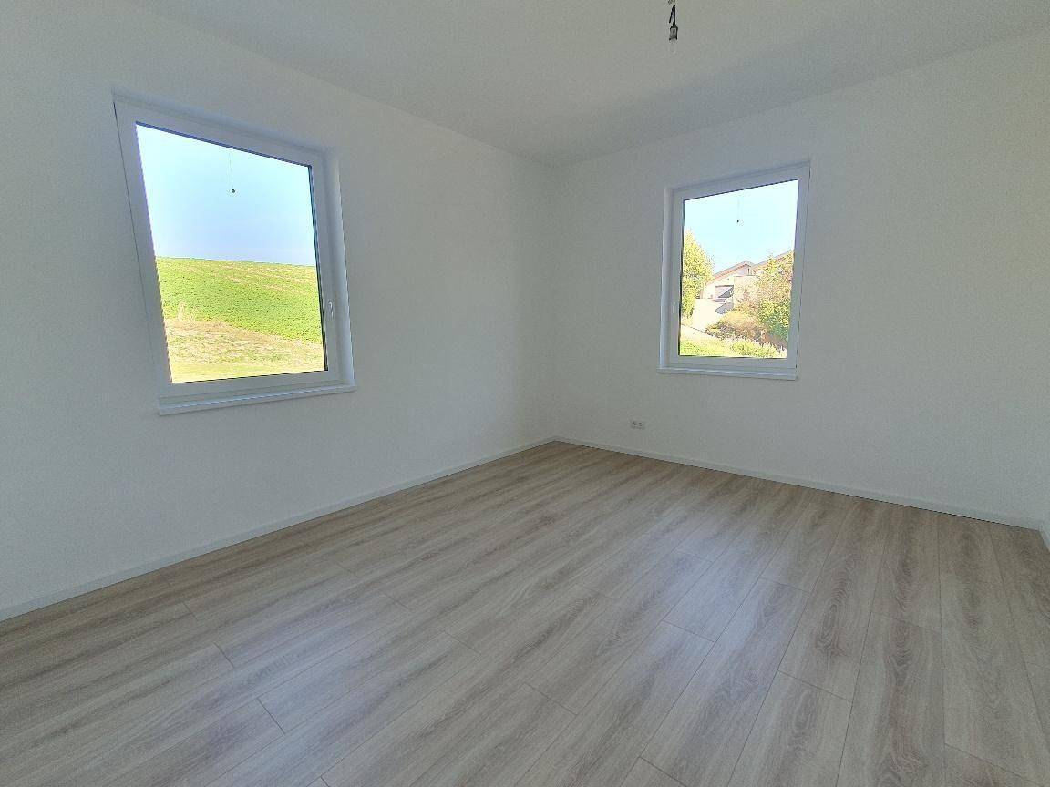 Geräumiger, heller Raum mit zwei Fenstern, Laminatboden und weitem Blick auf die Landschaft.