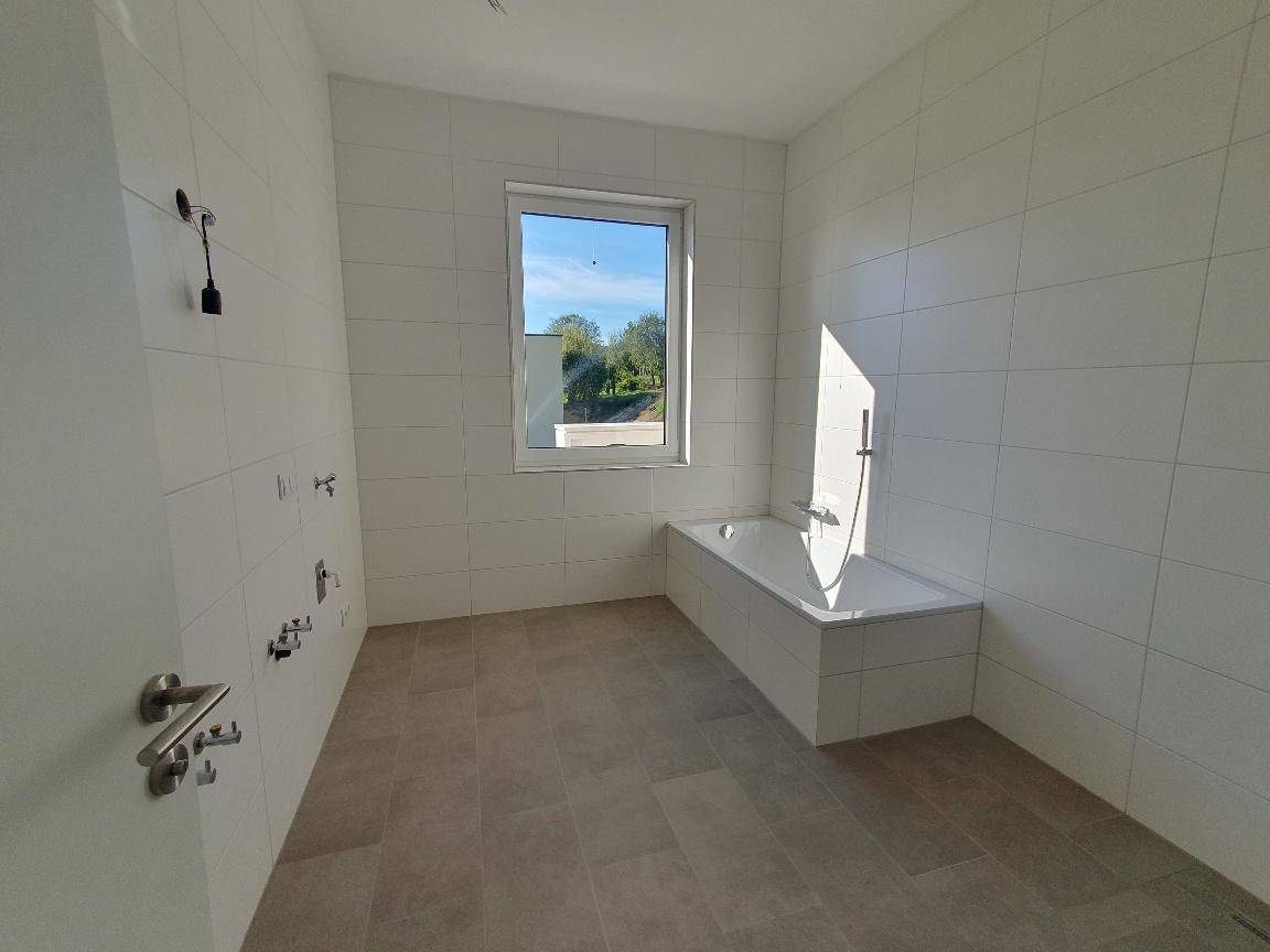 Modernes Badezimmer mit weißen Wandfliesen, einer Badewanne und einem Fenster für Tageslicht.