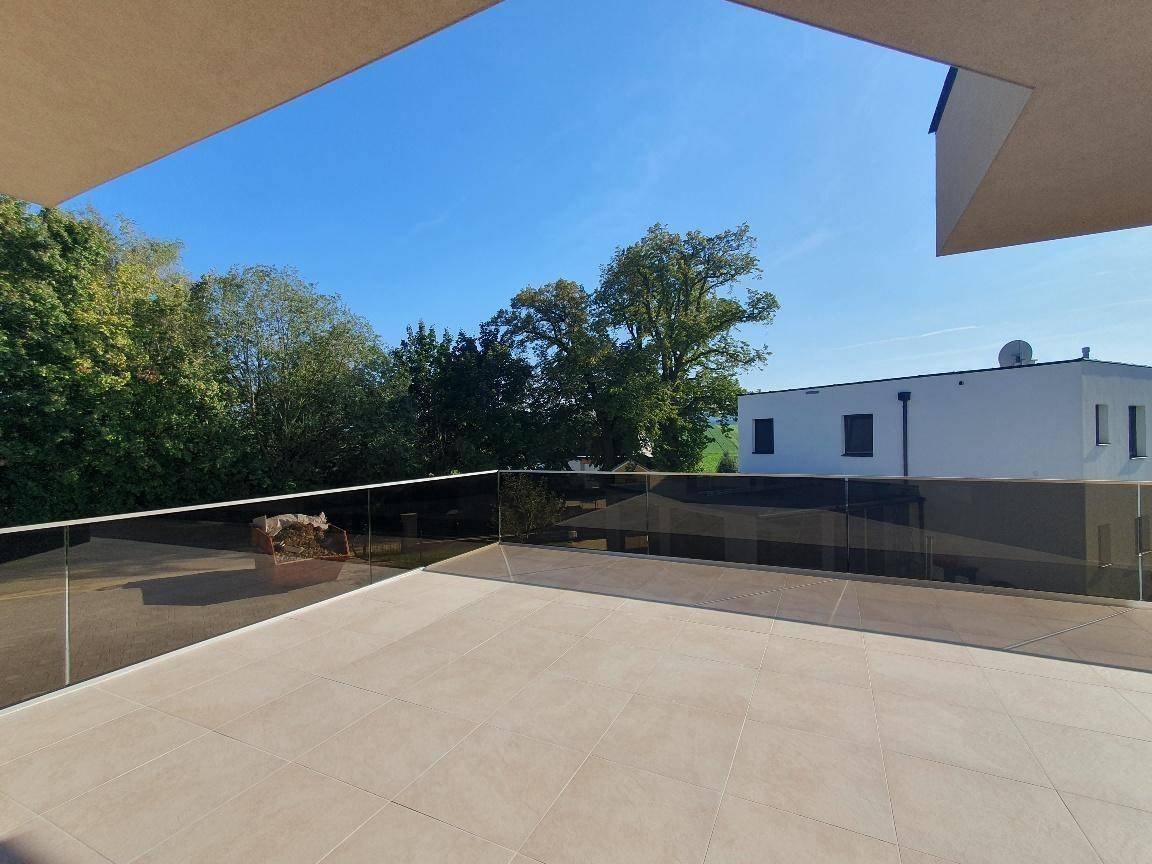 Großzügige Terrasse mit Fliesenboden und modernem Glasgeländer, umgeben von viel Grün.