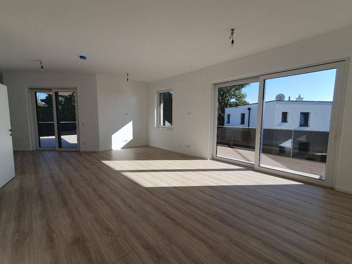 Heller, leerer Wohnbereich mit großen Schiebetüren, Laminatboden und viel Tageslicht.