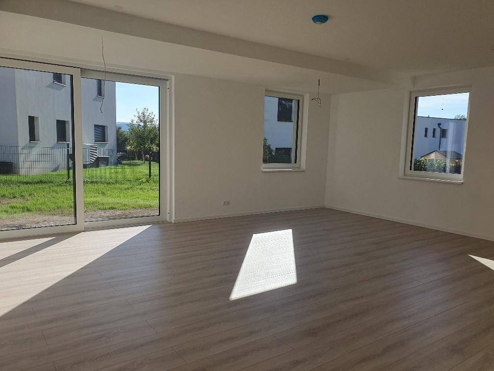 Geräumiger, lichtdurchfluteter Wohnraum mit Laminatboden und Blick ins Grüne durch große Fenster.