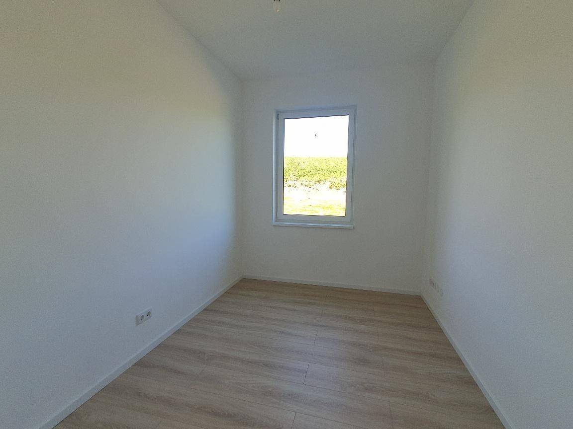 Kleiner, heller Raum mit Laminatboden und einem Fenster, das einen Blick ins Grüne bietet.