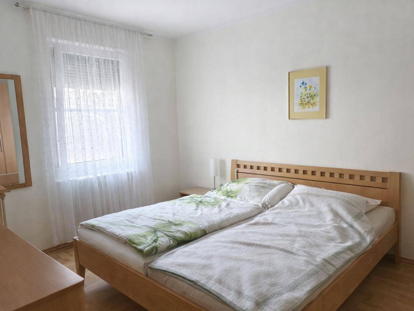 Helles Schlafzimmer mit Doppelbett, Holzrahmen und Fenster mit Vorhängen.
