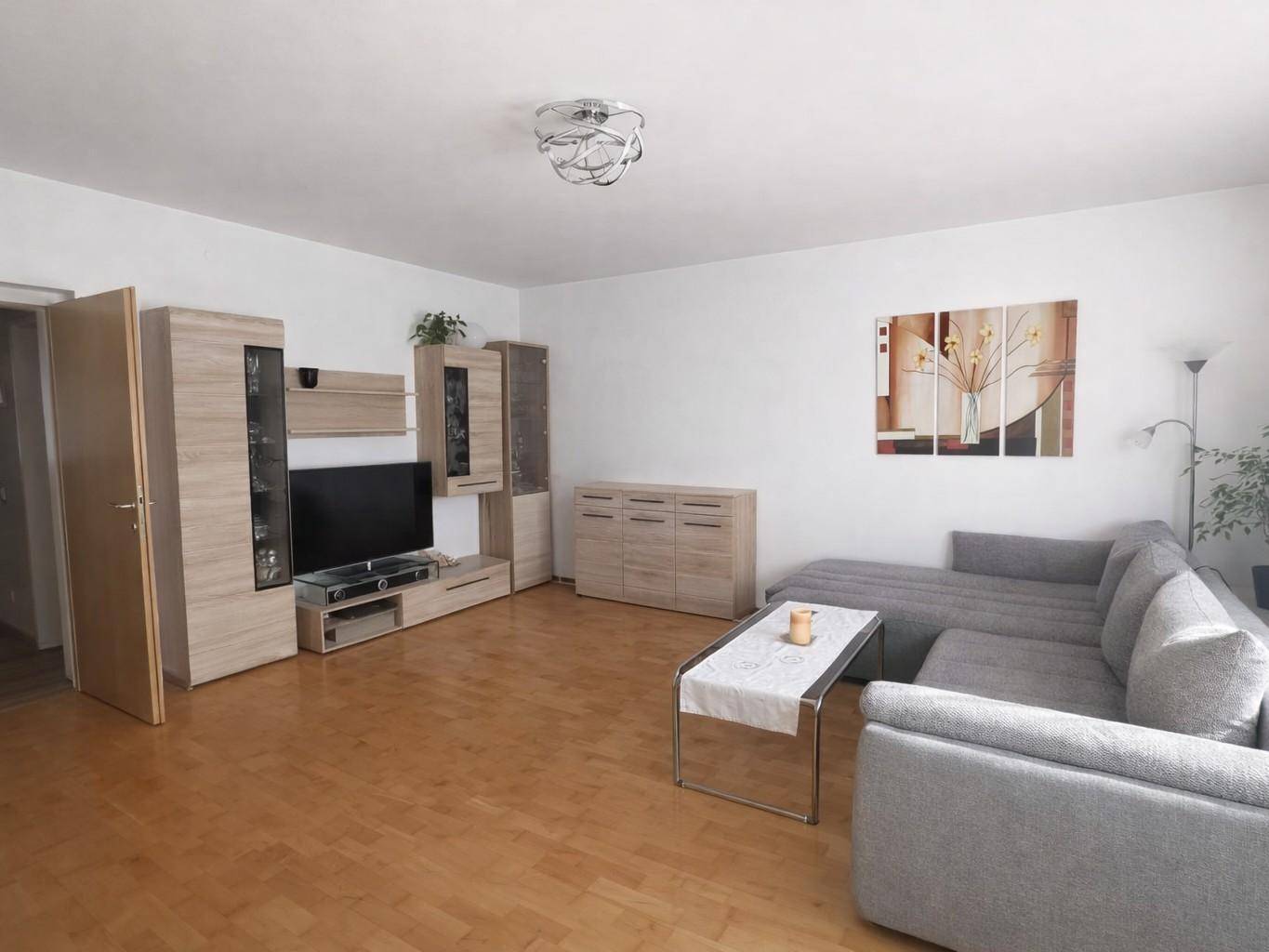 Geräumiges Wohnzimmer mit hellem Laminatboden, bequemer Couch und TV-Möbeln.