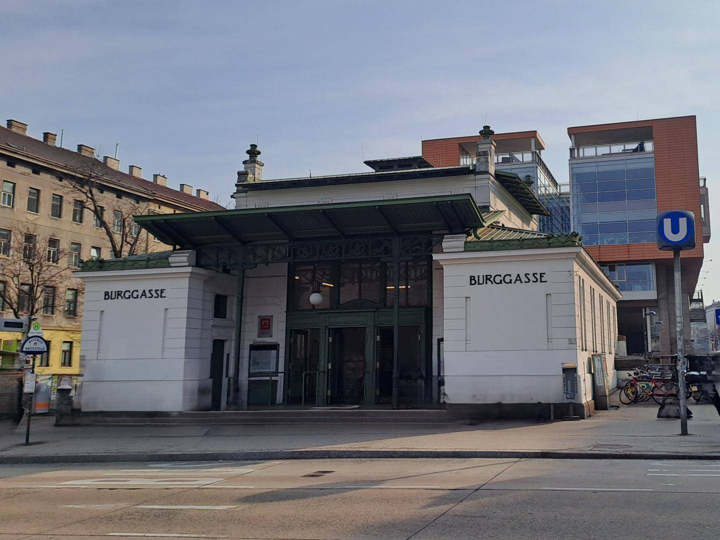 Historischer U-Bahn-Eingang "Burggasse" mit klassischer Architektur und modernen Gebäuden im Hintergrund.