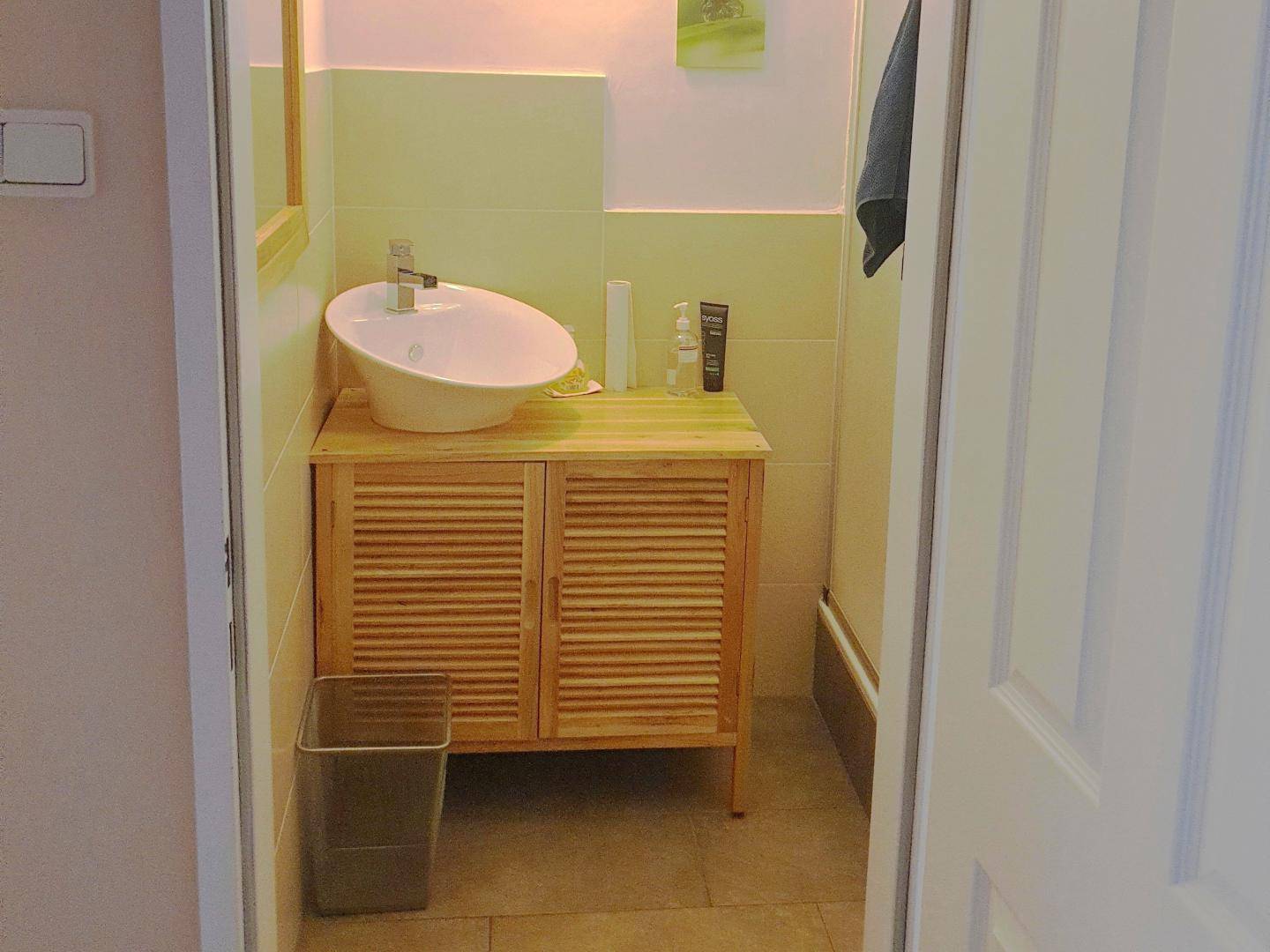 Modernes Badezimmer mit einem Holzwaschtischunterschrank, Aufsatzwaschbecken und hellen Fliesen.