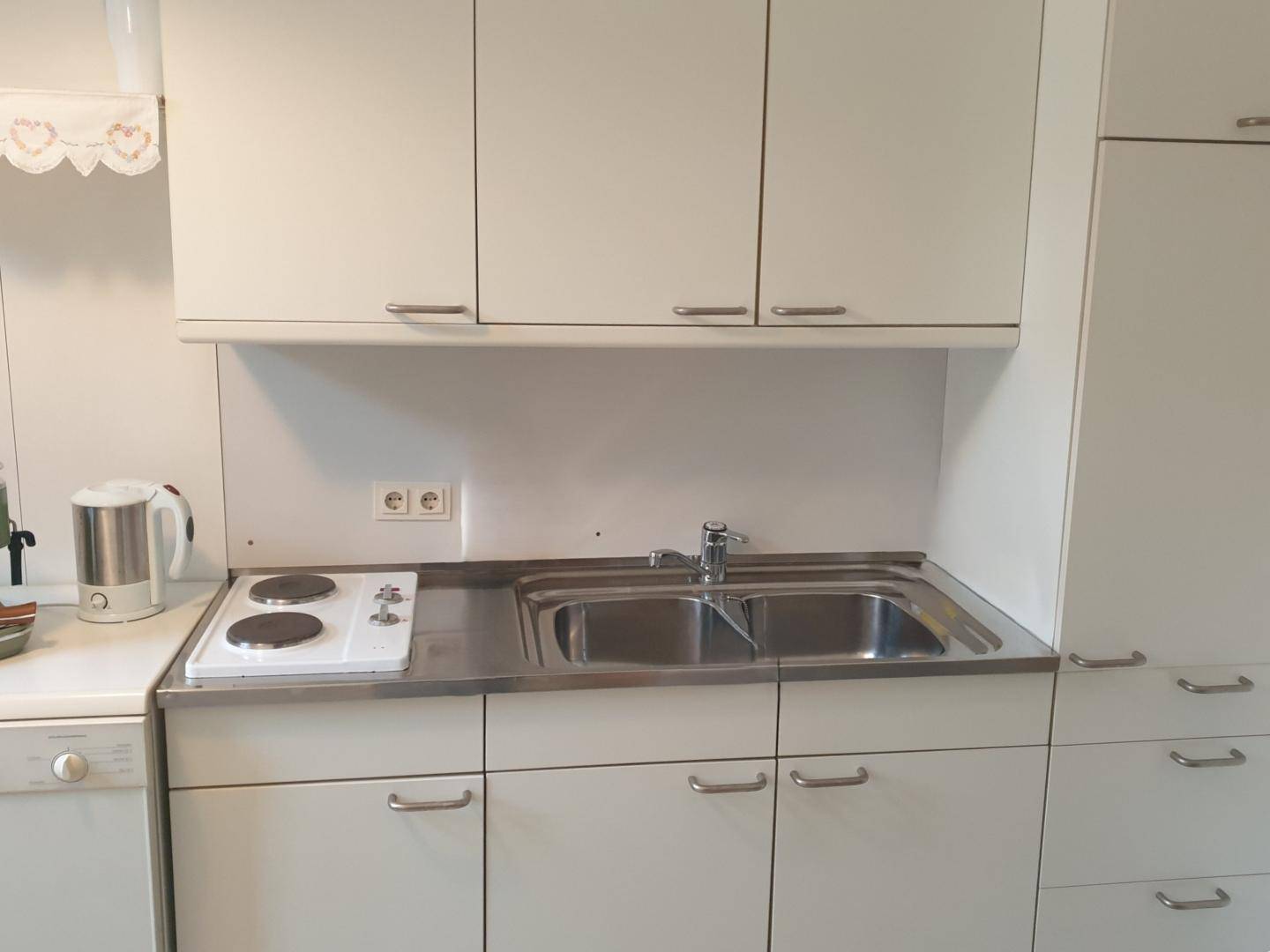 Nahaufnahme einer kompakten Küchenzeile mit weißen Schränken, Spüle und zwei Kochplatten.