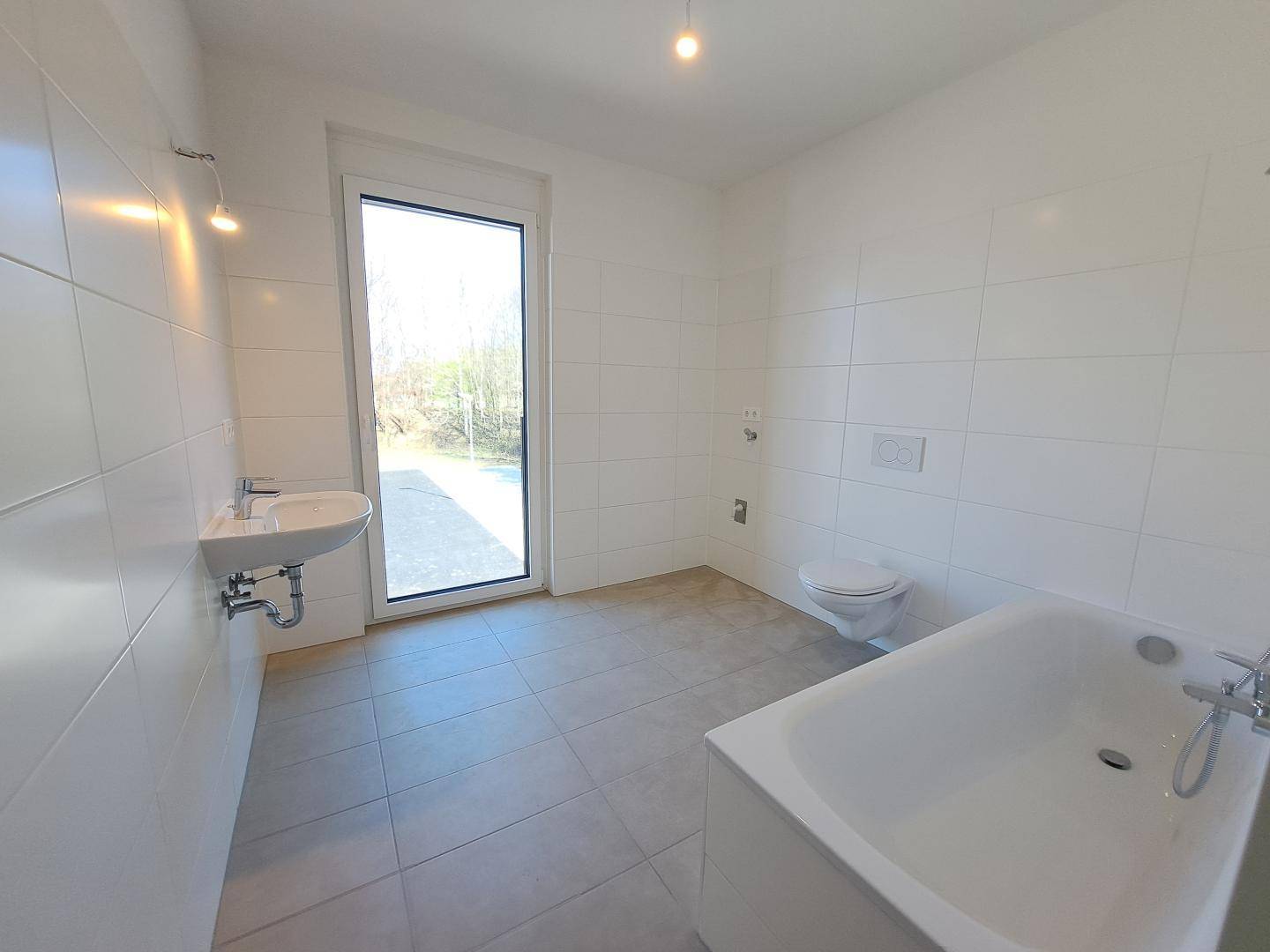 Modernes Badezimmer mit weißen Fliesen, Badewanne, wandhängendem WC und Fenster.