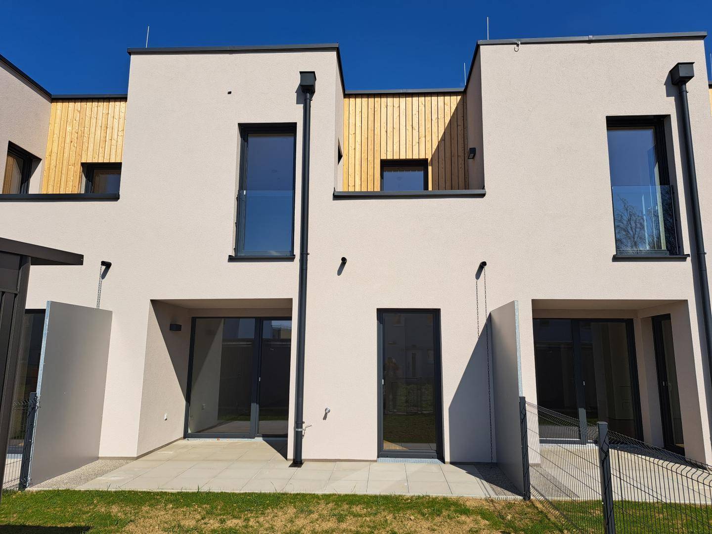 Moderne Reihenhäuser mit heller Fassade, Holzverkleidung und großen Fenstern.