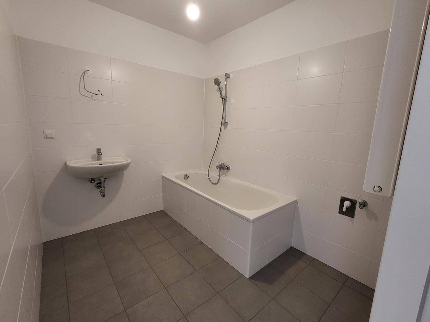 Modern gefliestes Badezimmer mit Badewanne, Duschfunktion und Waschbecken.
