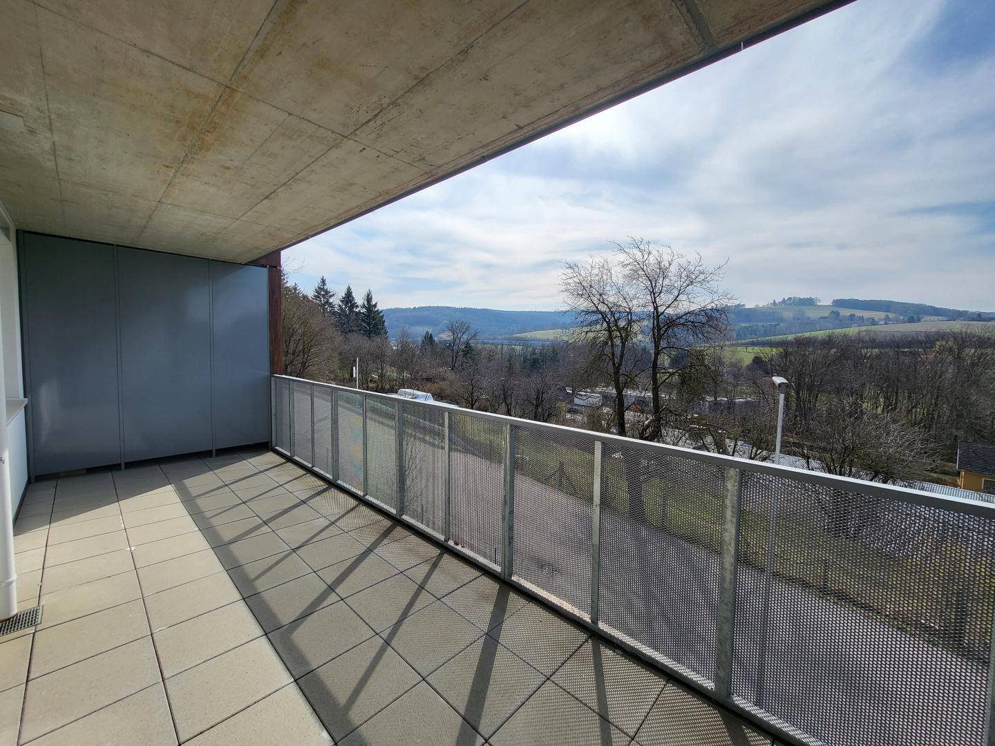 Geräumiger Balkon mit Fliesenboden und weitem Blick über die grüne Landschaft.