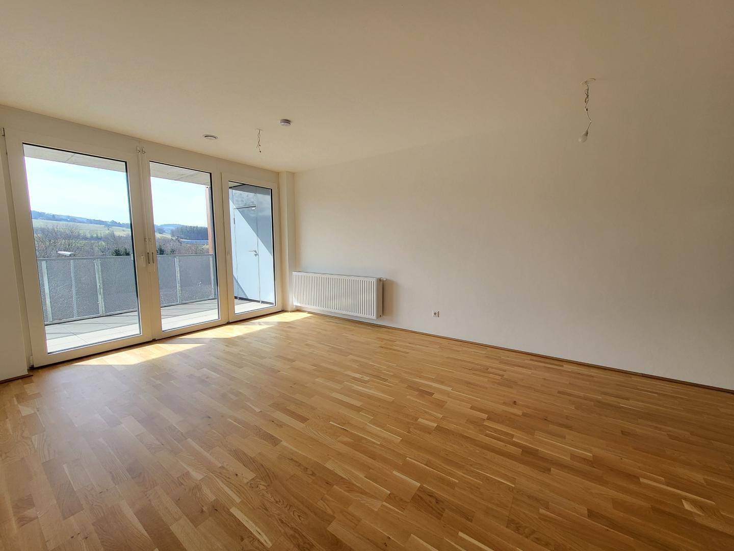 Helles Wohnzimmer mit großen Fenstern, Zugang zum Balkon und hochwertigem Parkettboden.