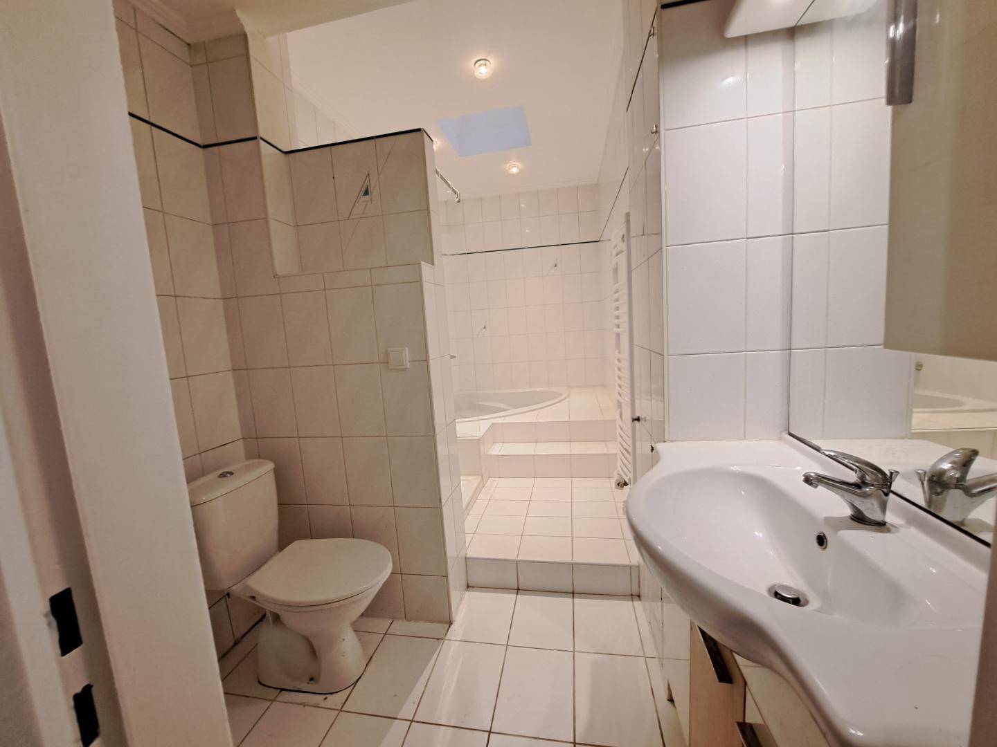 Gefliestes Badezimmer mit Toilette, Waschbecken und einer erhöhten Badewanne.