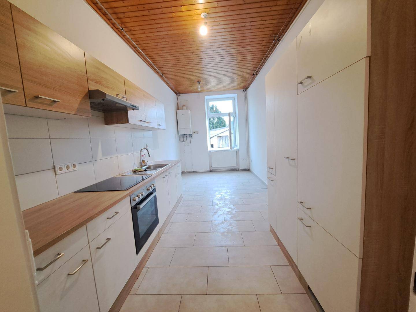 Funktionale Küche mit weißen Schränken, Holzarbeitsplatten und Holzdeckenverkleidung.