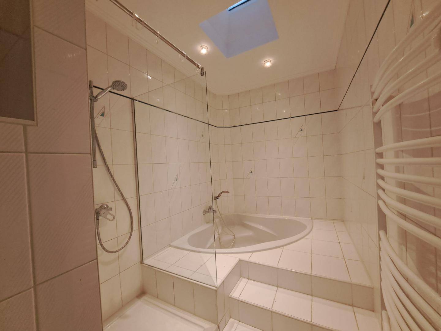 Modern gefliestes Badezimmer mit Badewanne, Dusche und beheiztem Handtuchhalter.