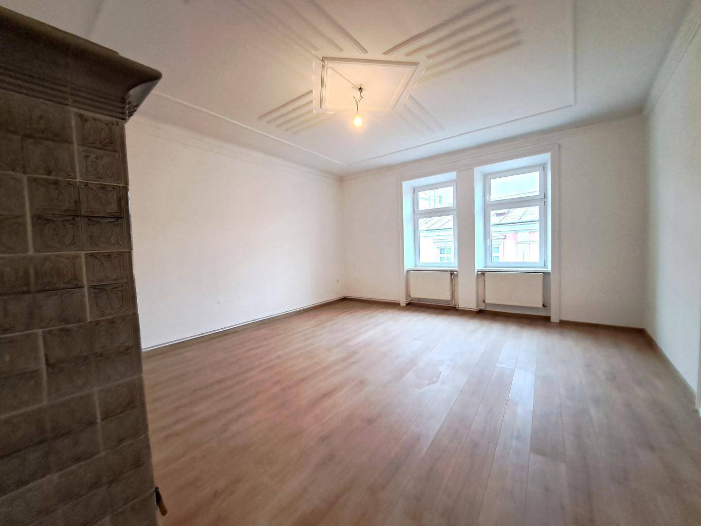 Heller Wohnraum mit zwei Fenstern, Laminatboden und dekorativer Decke.