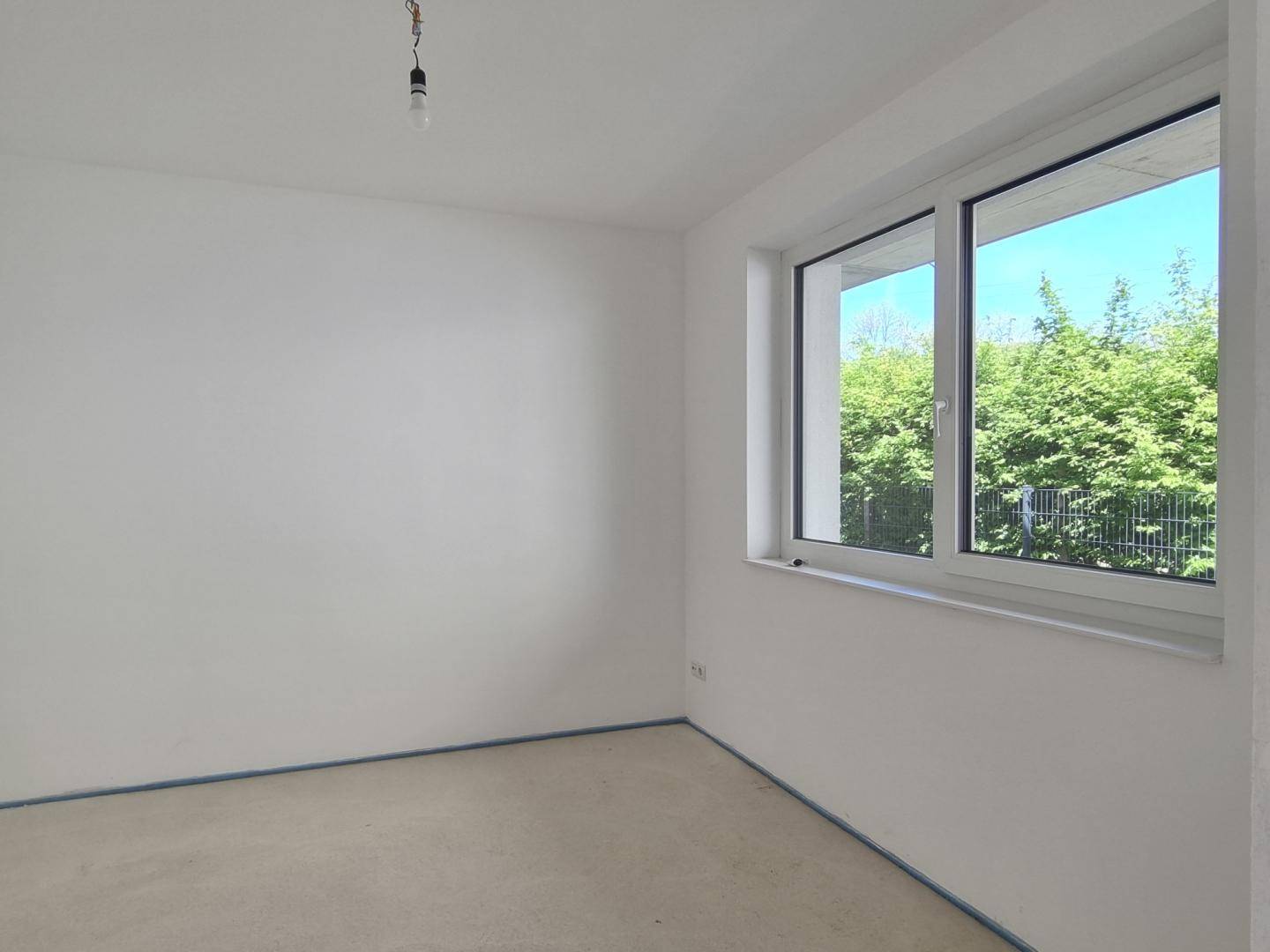 Unmöbliertes Schlafzimmer im Rohzustand mit großem Fenster und Blick ins Grüne.