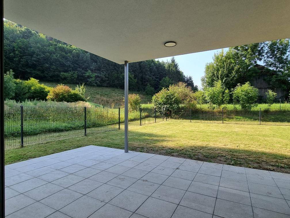Großzügige, gepflasterte Terrasse mit Blick auf die weitläufige Rasenfläche und bewaldete Hügel.