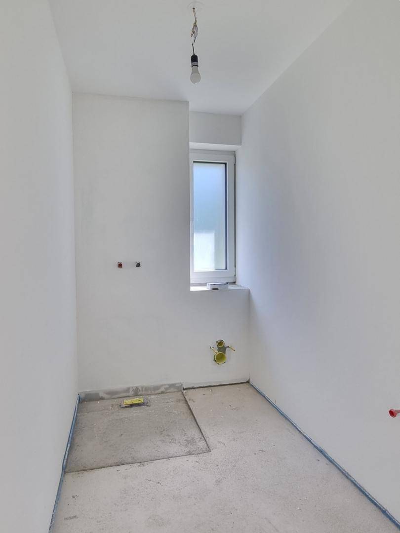 Kleiner Raum im Rohbau mit Fenster und vorbereiteten Anschlüssen für ein Gäste-WC.