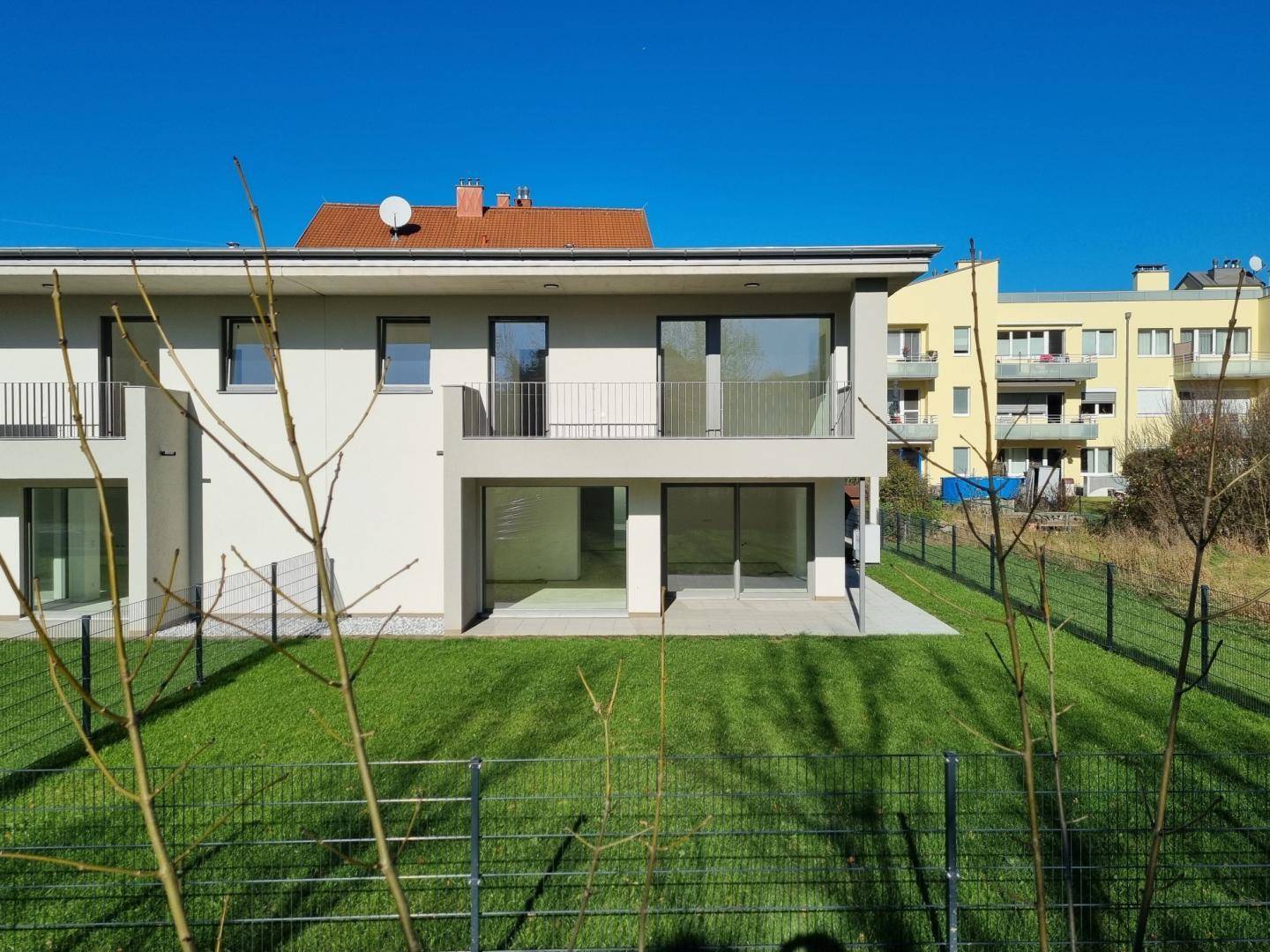 Moderne Doppelhaushälfte mit großen Fensterfronten und Zugang zum Garten, umgeben von viel Grün.