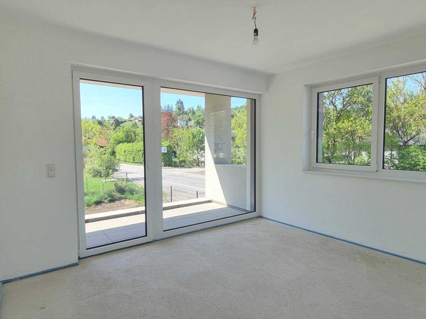 Helles Schlafzimmer im Rohbau mit großem Fenster und Zugang zum Balkon.