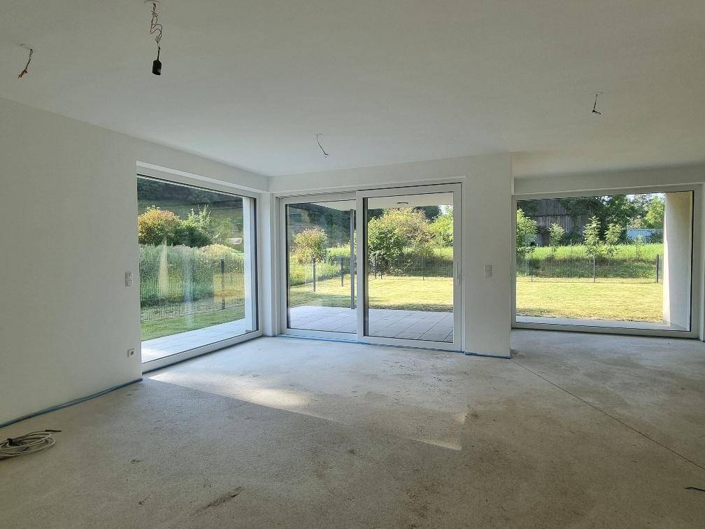 Unmöblierter Wohnbereich mit großen Schiebetüren, die viel Licht hereinlassen und Zugang zum Garten bieten.