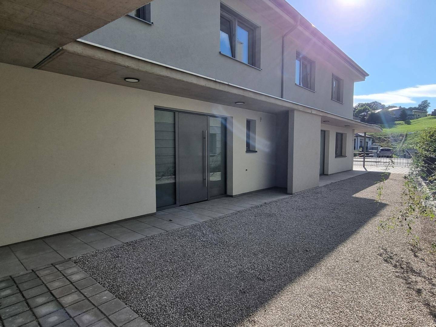 Moderner Eingangsbereich des Doppelhauses mit gepflastertem Weg und Kiesfläche.