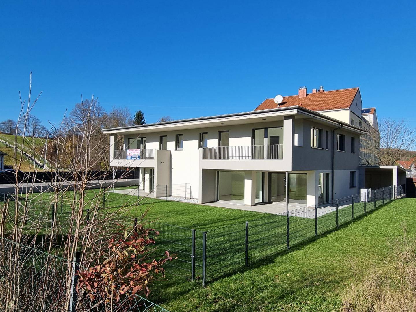Neubau-Doppelhaushälfte mit moderner Architektur, großen Fenstern und umlaufendem Gartenbereich.