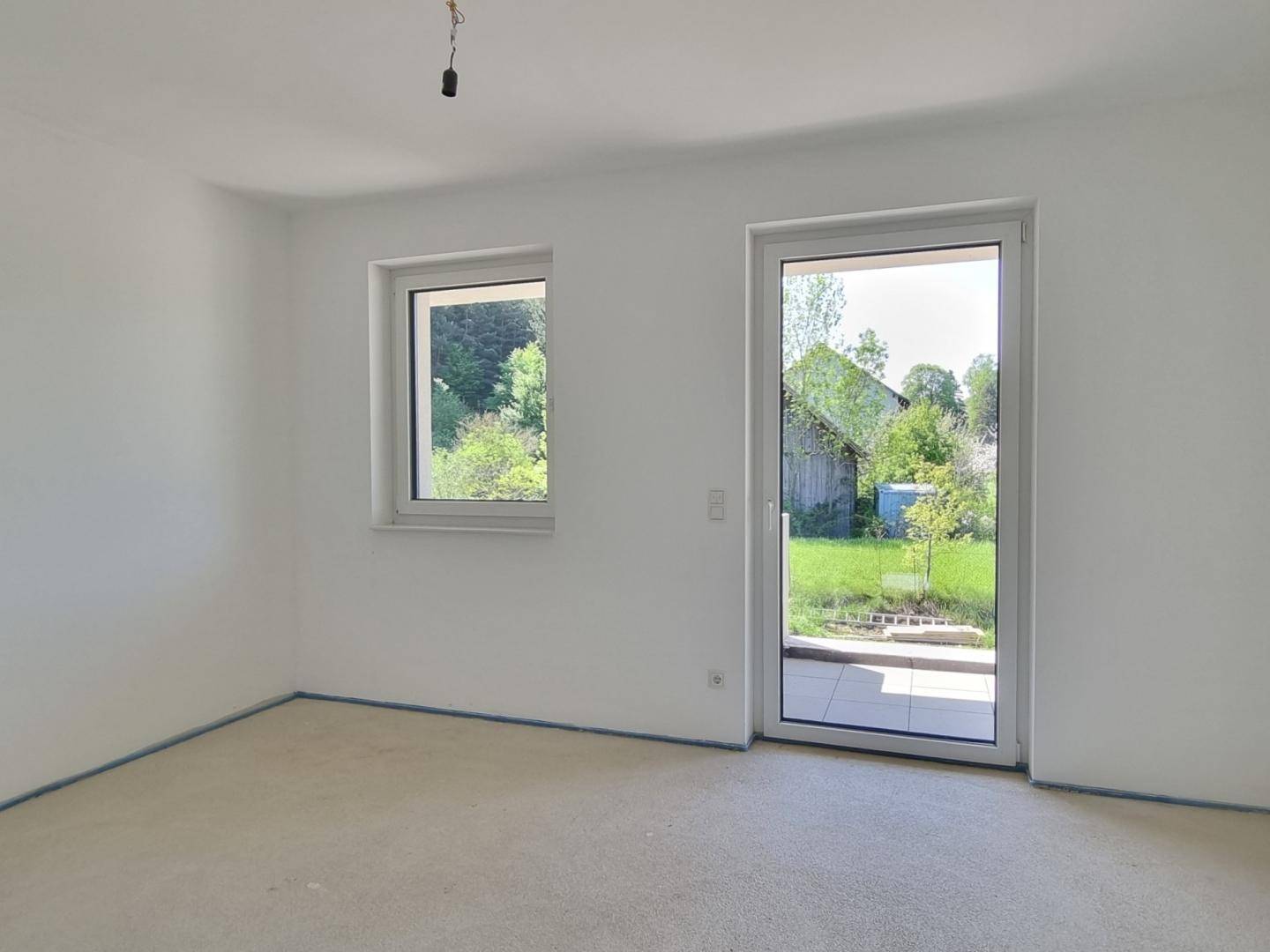 Unmöbliertes Zimmer im Rohzustand mit Fenster und direktem Zugang zum Gartenbereich.