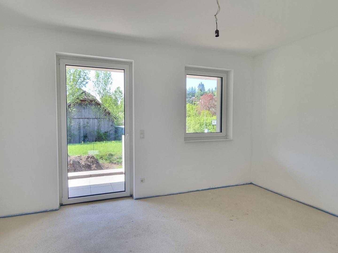 Helles Zimmer im Rohzustand mit Fenster und direktem Zugang zum Gartenbereich.