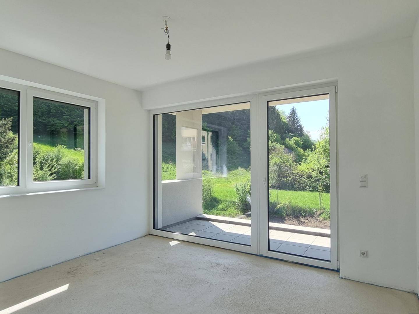 Unmöbliertes Schlafzimmer im Rohbau mit großzügiger Fensterfront und Zugang zum Balkon.