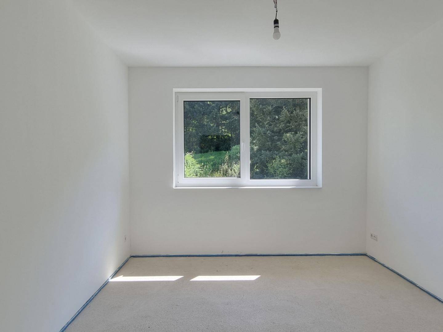 Helles Schlafzimmer im Rohzustand mit großem Fenster und Blick ins Grüne.