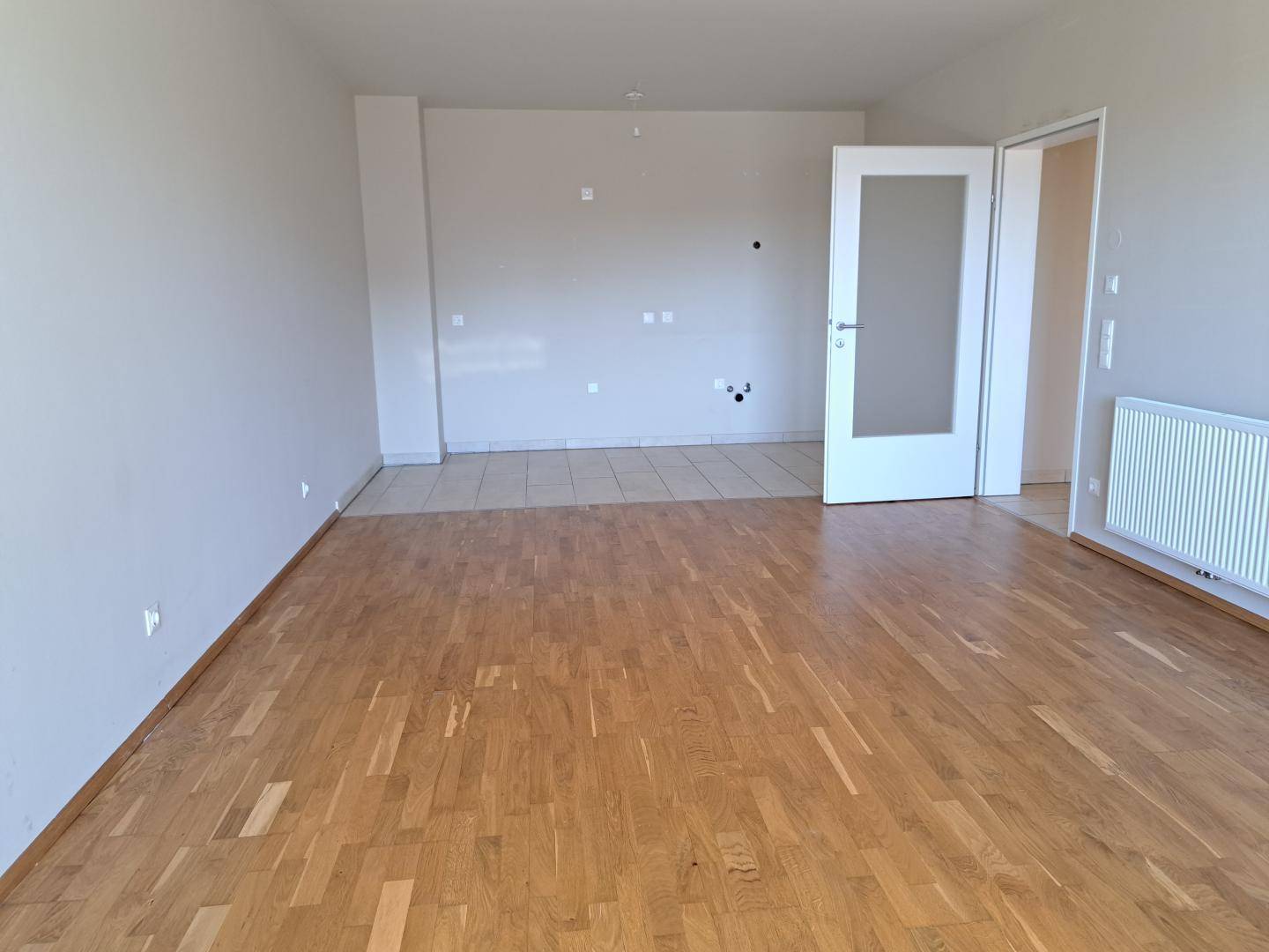 Heller, leerer Raum mit Parkettboden und Fliesenbereich, ideal für einen offenen Wohn-Essbereich.