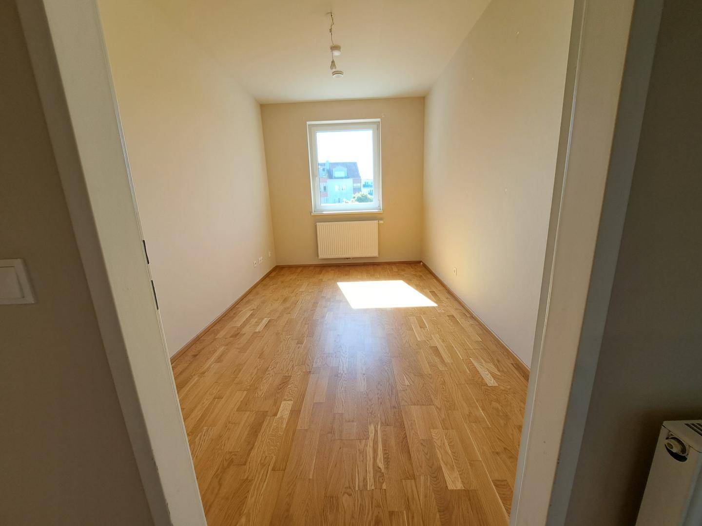 Geräumiges Schlafzimmer mit hellem Parkettboden und Fenster, das den Raum gut belichtet.