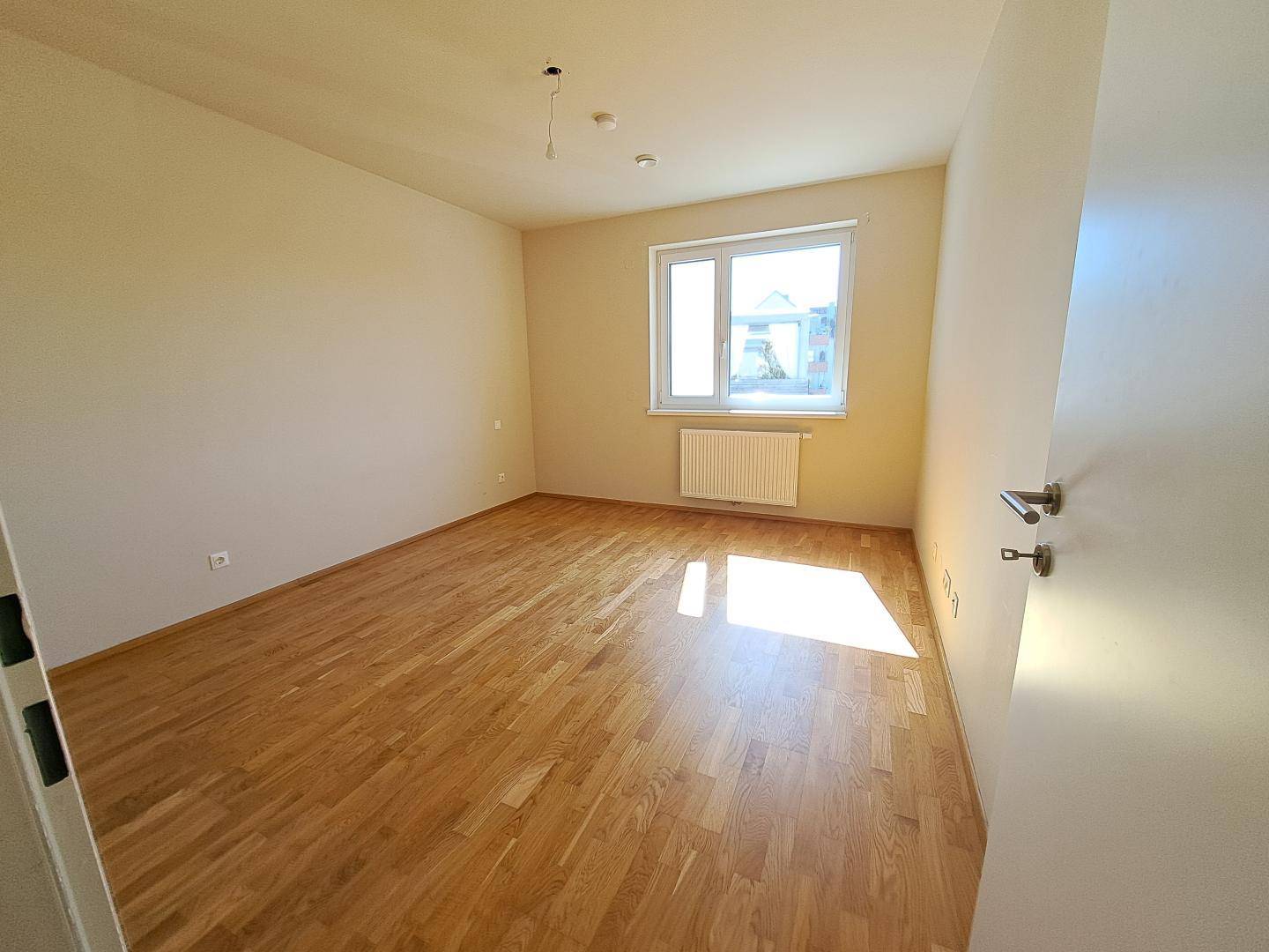 Helles Schlafzimmer mit Eichenparkettboden und großem Fenster, das viel Tageslicht hereinlässt.