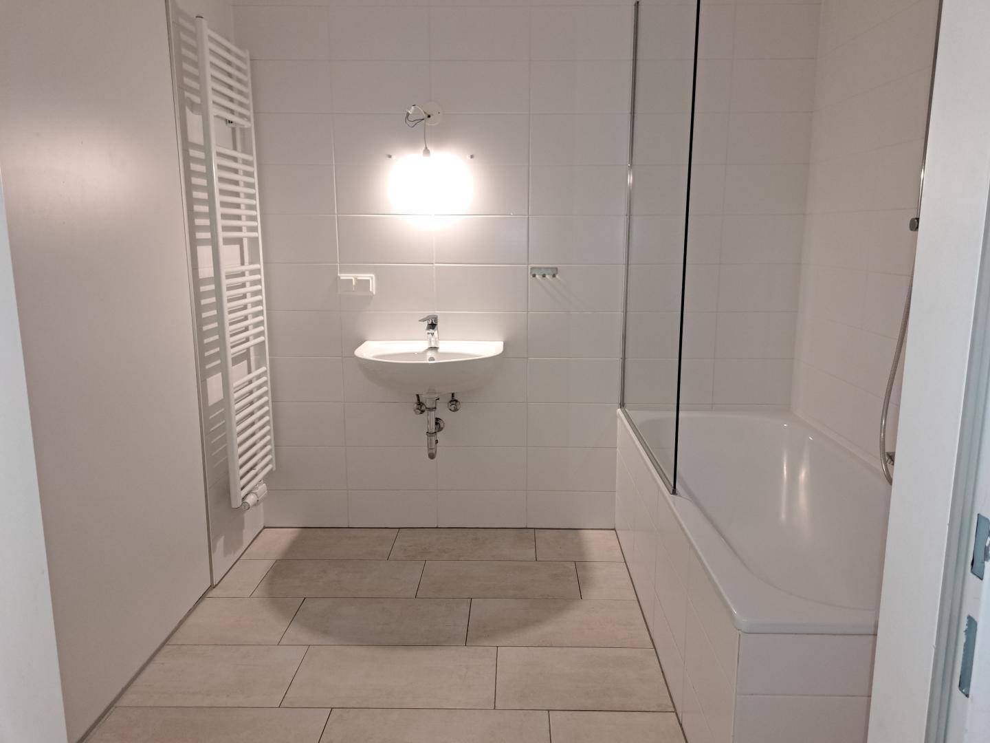 Modernes Badezimmer mit weißen Fliesen, Badewanne mit Duschwand und beheiztem Handtuchhalter.