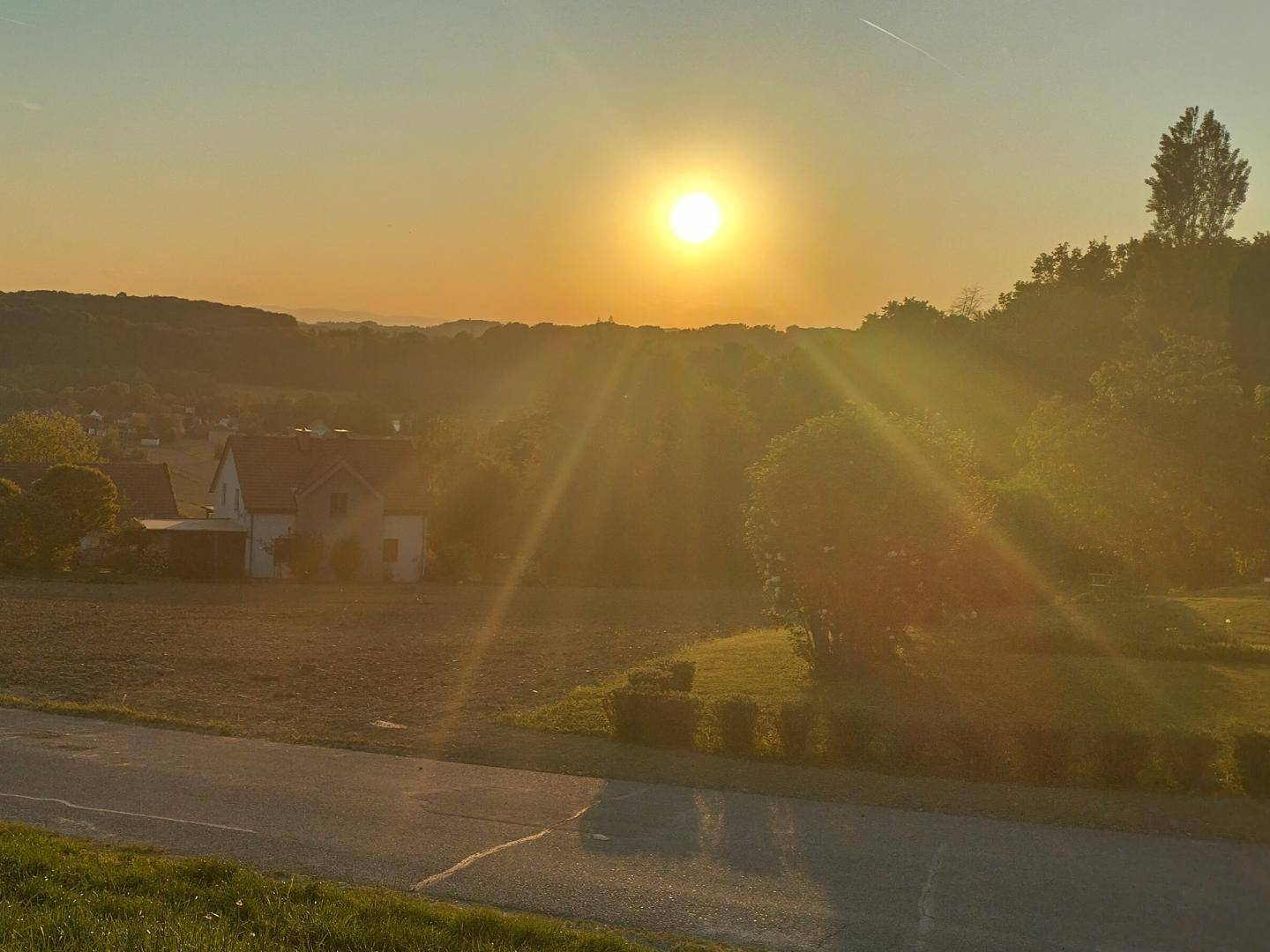 Spektakulärer Sonnenuntergang über einer ländlichen Landschaft mit Häusern und weiten Feldern im warmen Abendlicht.